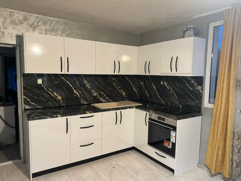 White L-shaped kitchen with a dramatic black marble-effect splashback
